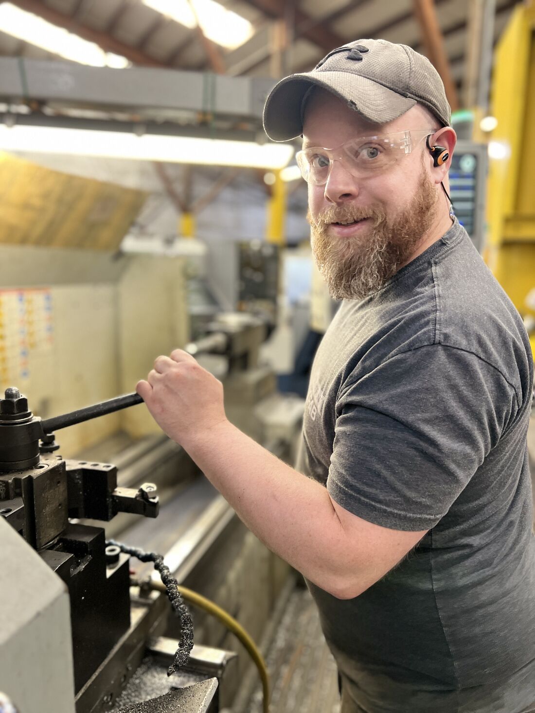 A machinist in safety glasses works at a lathe on an Everett shop floor