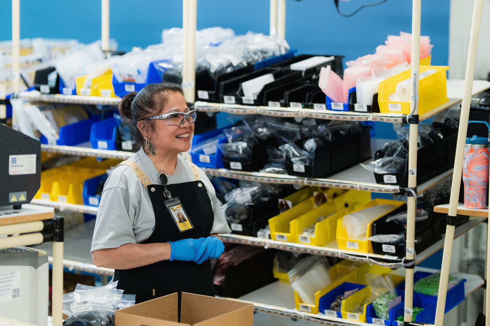 A smiling worker in safety glasses and gloves kitting precision components at an Everett production bench